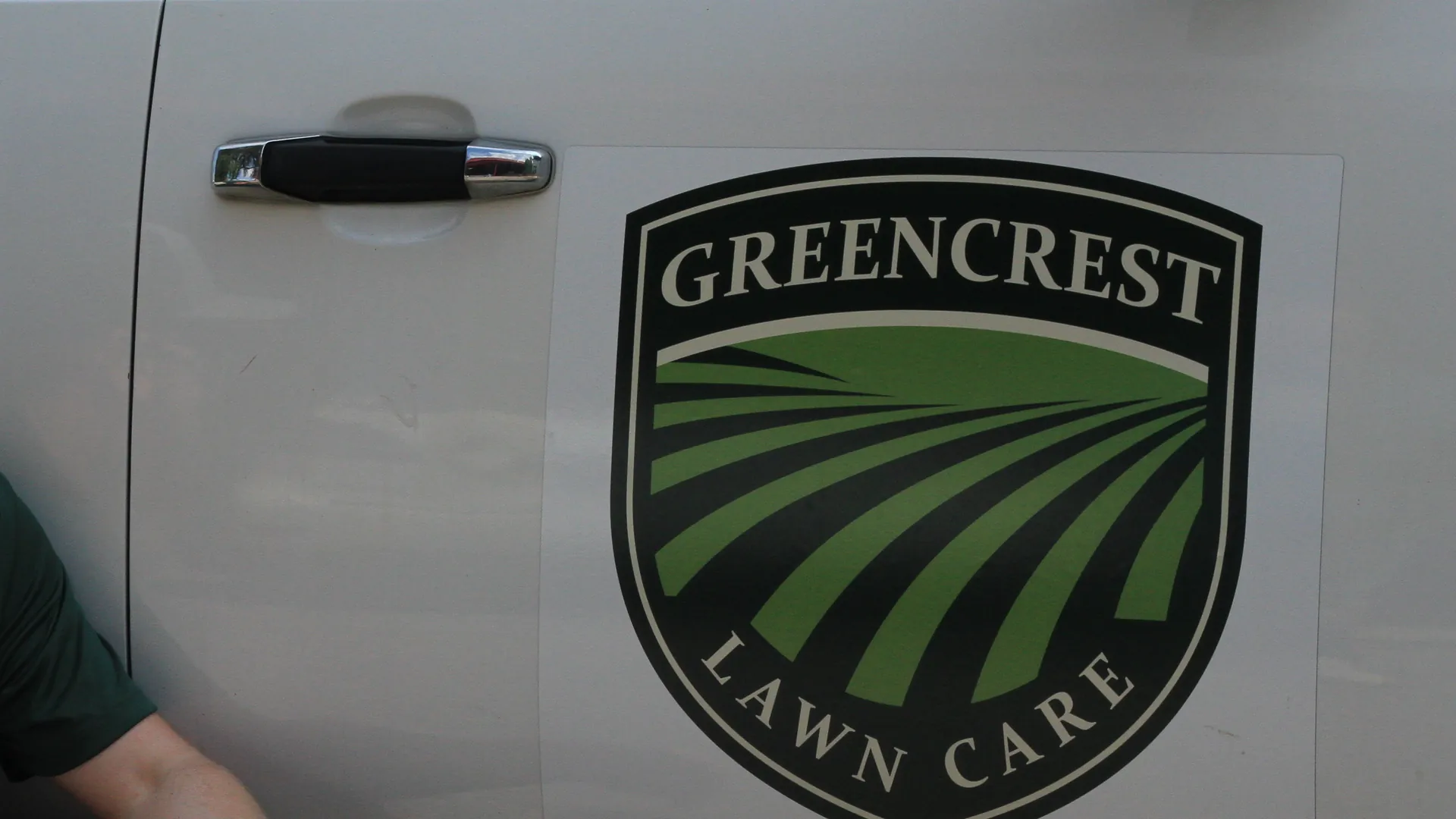 The Greencrest Lawn Care shield and phone number on the door of Chris's work truck
