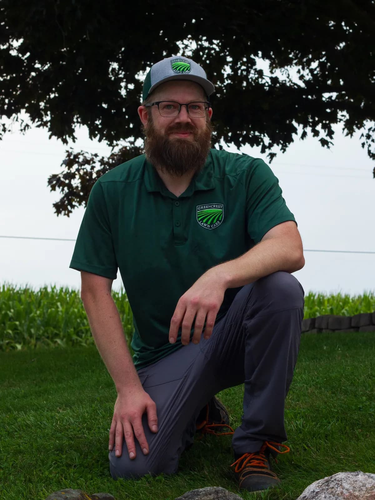 Chris, the owner of Greencrest Lawncare, kneeling on a mown lawn in front of a corn field