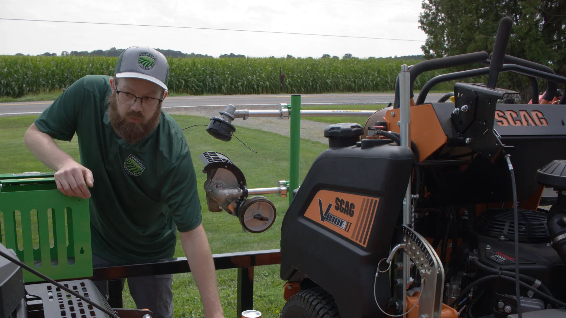 Chris, in his Greencrest cap and polo, leaning on the back of his trailer beside two stand-on mowers