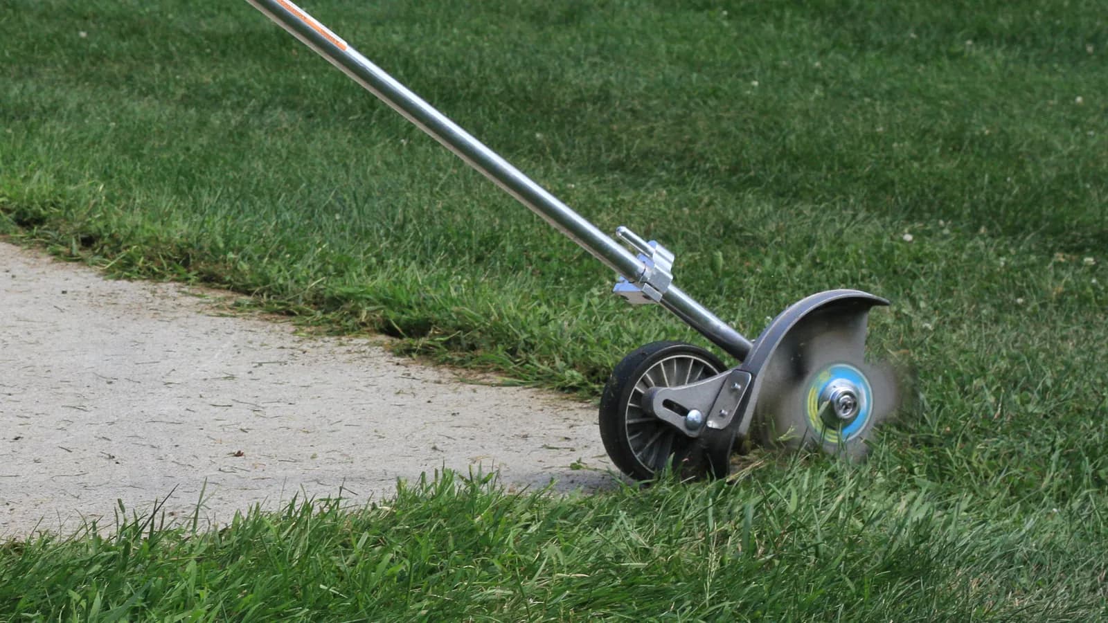 An edger blade cutting a sharp line where turf meets a concrete walk